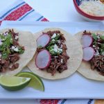 3 tacos on a white plate with lime wedges
