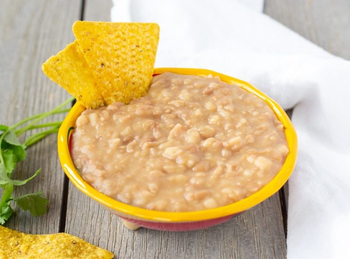 Refried Peruvian beans in a small yellow bowl with tortilla chips on the side.