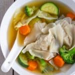 Wonton and Vegetables in a white bowl with a white soup spoon inside.