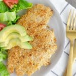 Chicken milanesa on a white plate with a side salad.