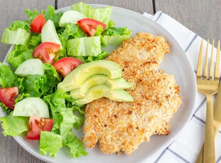 Chicken milanesa on a white plate with a side salad.