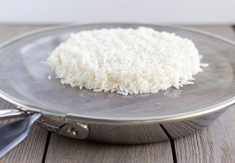 Saute pan with splatter guard as the cover, and a mound of sticky rice on top.