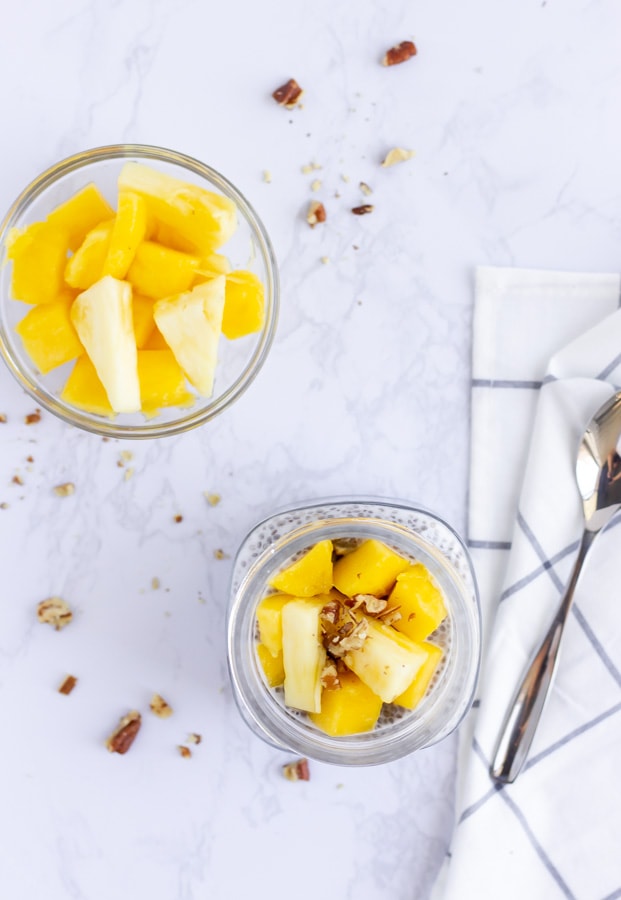 Overhead view of chia pudding with mango and pineapple on top and crushed nuts on a white marble background.