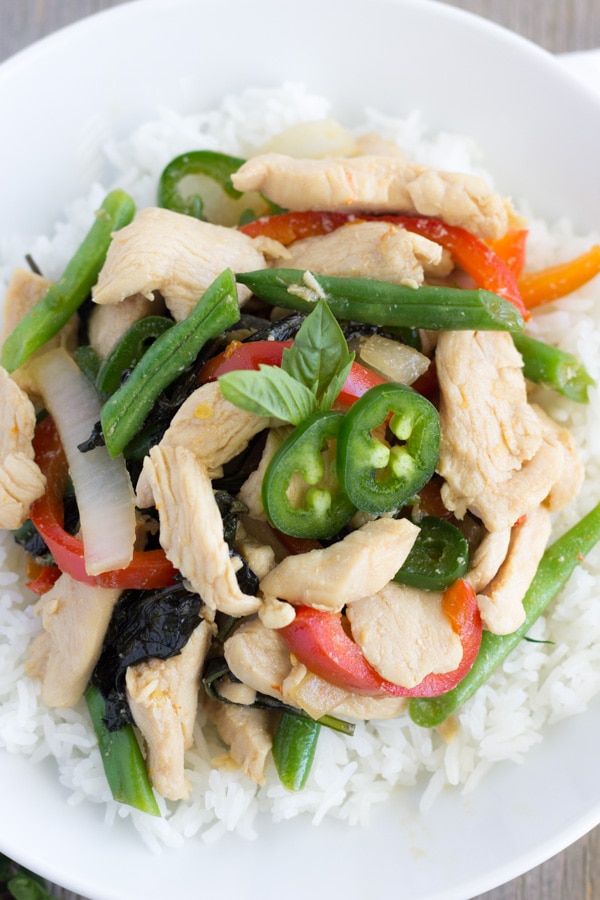 White bowl with rice on the bottom and spicy basil chicken on top.