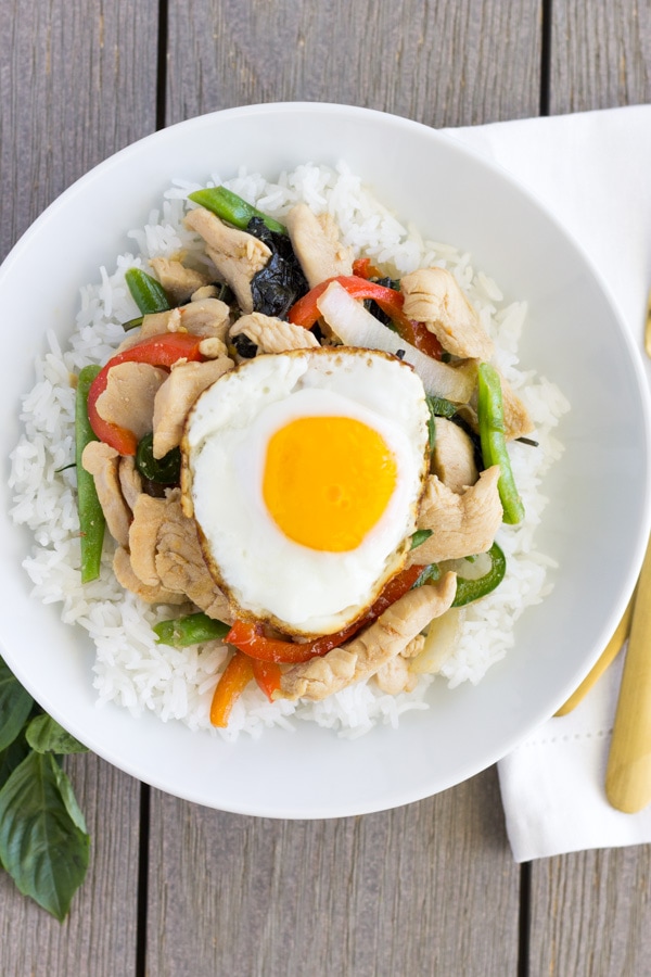 White bowl with rice on the bottom and spicy basil chicken on top with a fried egg.