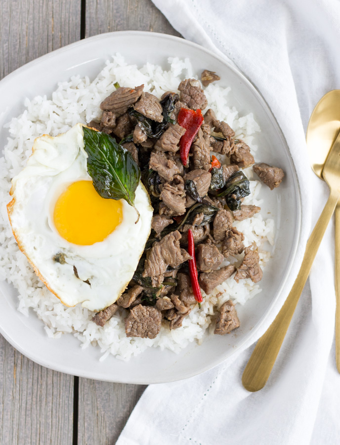 Thai Beef Basil on a white plate with rice and a fried egg on the side.