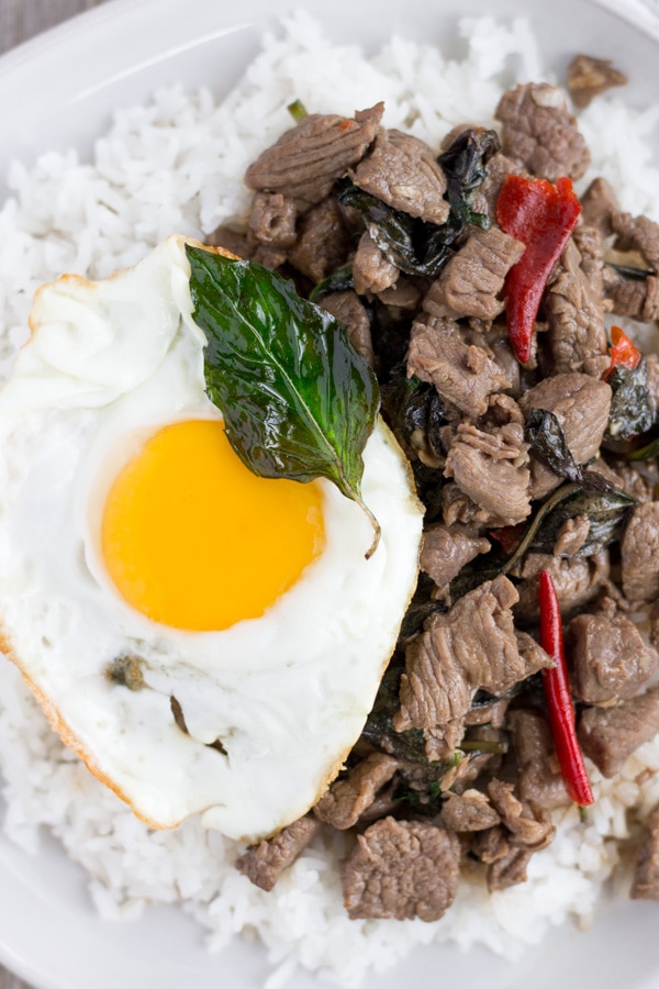 Thai Beef Basil on a white plate with rice and a fried egg on the side.