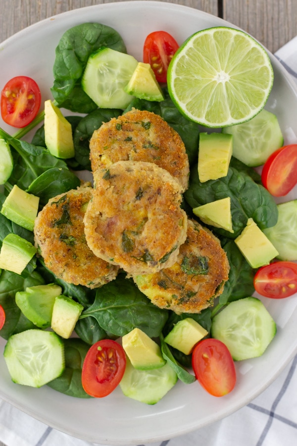 Avocado Cilantro Tuna Cakes on a bed of spinach with sliced cucumbers, tomatoes, and avocado.